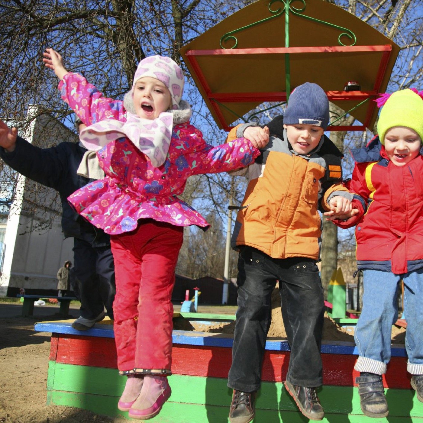 Drei Kinder springen fröhlich von einer Bank